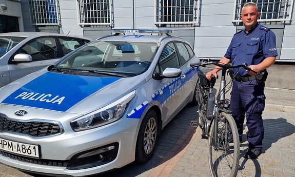 umundurowany policjant z odzyskanym rowerem, obok stroi radiowóz