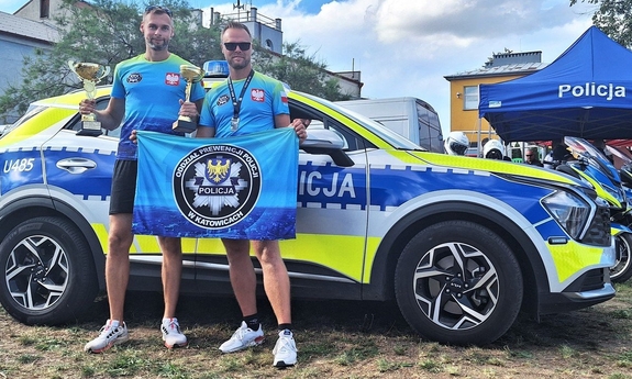 policjanci w strojach sportowych z pucharami, w tle oznakowany radiowóz