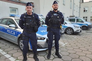 Na tle radiowozu stoi dwóch policjantów.