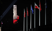 Pora nocna. Podświetlony na biało-czerwono pomnik na Westerplatte. Po prawej stronie flagi Polski, Unii europejskiej i Miasta Gdańska na masztach.