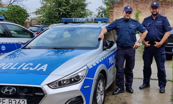 dwóch umundurowanych policjantów stoi przy radiowozie