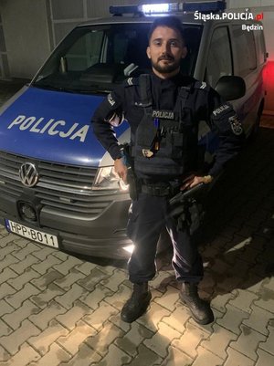 Umundurowany policjant stoi na tle radiowozu