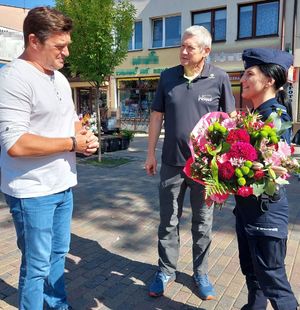 umundurowana policjantka z bukietem kwiatów, obok niej stoi dwóch mężczyzn