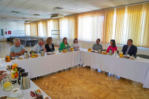 Grupa przedstawicieli gości i gospodarzy siedzi przy stoliku w dużym pomieszczeniu służbowym