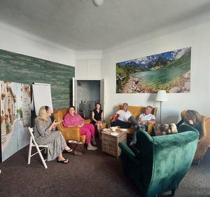 Grupa rozmawiająca w  pomieszczeniu fundacji. Osoby siedzą wokół małego stolika