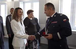 I zastępca Komendanta Głównego Policji nadinsp. Dariusz Augustyniak gratuluje kobiecie podając rękę, w tle policjanci