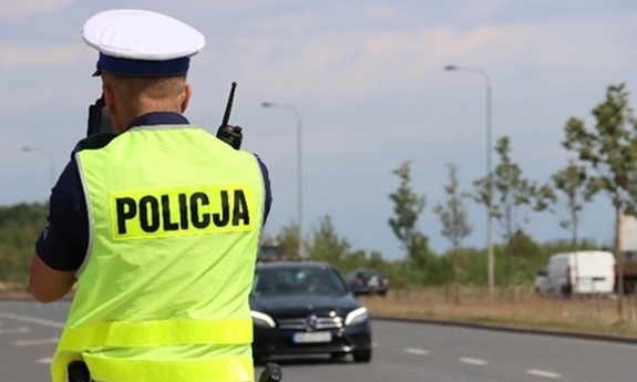 policjant ruchu drogowego stoi przy drodze, w tle jadący samochód
