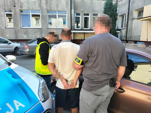 dwaj policjanci z zatrzymanym mężczyzną przy nieoznakowanym radiowozie
