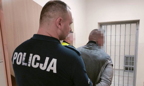 policjant prowadzi zatrzymanego mężczyznę zakutego w kajdanki