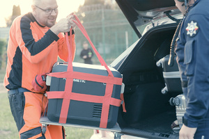 Ratownik medyczny wyjmuje z samochodu pojemnik do transportu organów, obok członek załogi policyjnego śmigłowca.