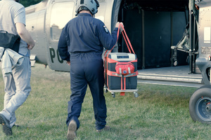 Pilot niesie pojemnik do transportu organów w kierunku oczekującego śmigłowca, z nim podąża mężczyzna.