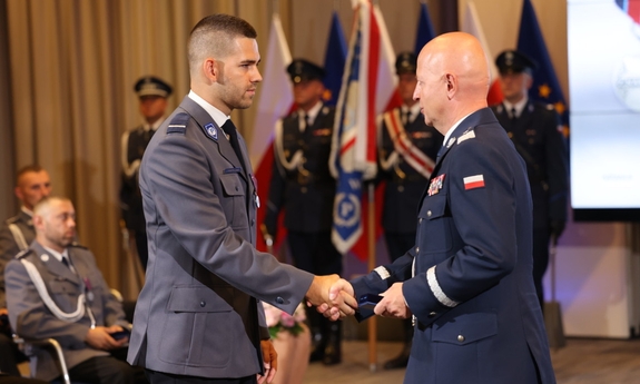 policjant odbiera medal z rąk komendanta głównego Policji