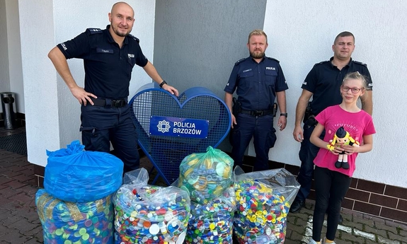 trzej policjanci stoją razem z dziewczynką przy workach z nakrętkami