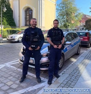 dwaj policjanci stoją przed radiowozem policyjnym