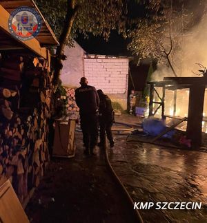 policjanci z wężem strażackim, w głębi płonący budynek
