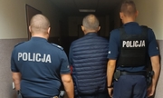 dwaj umundurowani policjanci prowadzą korytarzem zatrzymanego mężczyznę