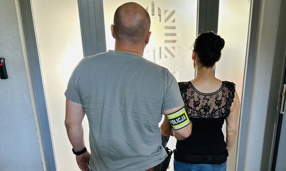 policjant kryminalny trzyma zatrzymaną kobietę w budynku komendy