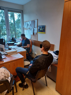 Policjant siedzi przy biurku przesłuchując zatrzymanego mężczyznę, który siedzi na krześle