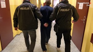 dwóch policjantów prowadzi zatrzymanego podejrzanego o zabójstwo