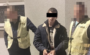 dwaj policjanci prowadza zatrzymanego mężczyznę zakutego w kajdanki