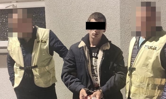 dwaj policjanci prowadza zatrzymanego mężczyznę zakutego w kajdanki