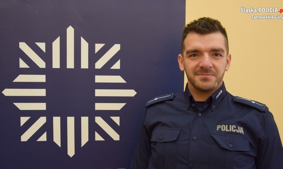 dzielnicowy Łazaj przy banerze z napisem policja