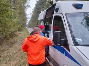 trzej mężczyźni stoją przy radiowozie na drodze w lesie