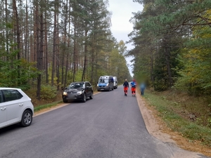 na drodze leśnej stoją dwa radiowozy i inne samochody, drogą idą trzej mężczyźni