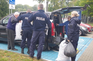 policjanci pakują nakrętki do pojazdu w tle parking przy jednostce