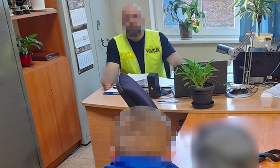policjant siedzi przy biurku, przesłuchuje zatrzymanego