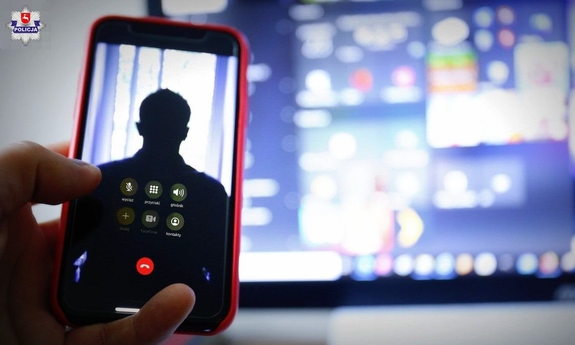telefon trzymany w ręku, w tle widać ekran monitora