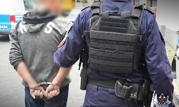 policjant prowadzi zatrzymanego zakutego w kajdanki