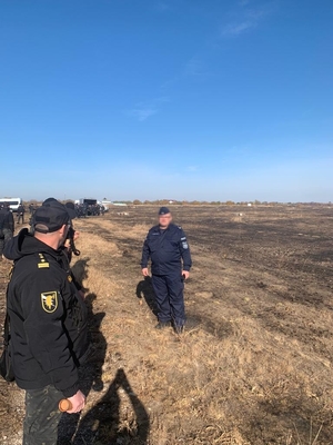 Otwarta przestrzeń. Policjant stoi naprzeciwko funkcjonariuszy stojących w rzędzie.