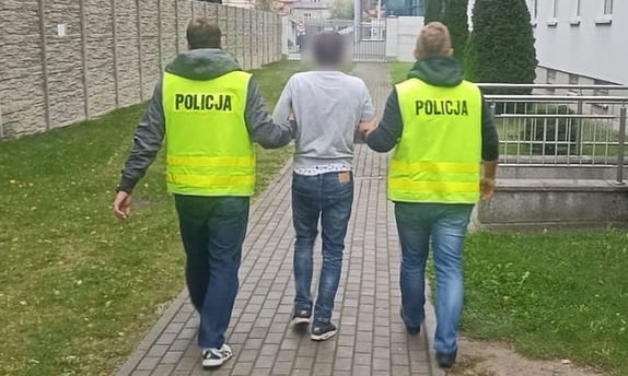 Policjanci w kamizelkach z napisem Policja prowadzą zatrzymanego mężczyznę