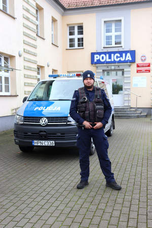 policjant stoi przed radiowozem policyjnym, w tle budynek komendy Policji w Bytowie