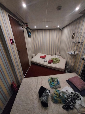 Wnętrze escapetrucka stylizowane na pokój. Na podłodze leżą dwa materace z porozrzucanymi ubraniami, po prawej stronie na ścianie umywalka i lustro.