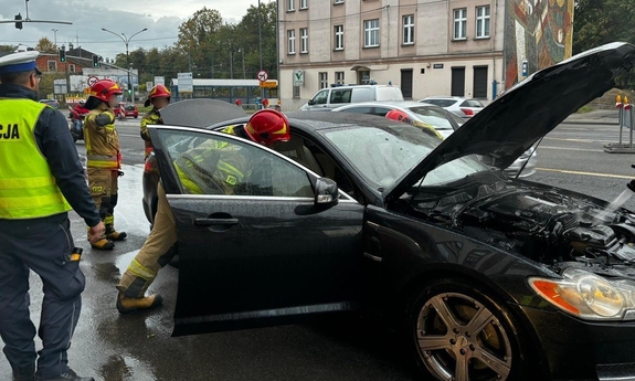 policjant i strażacy podczas gaszenia palącego się samochodu