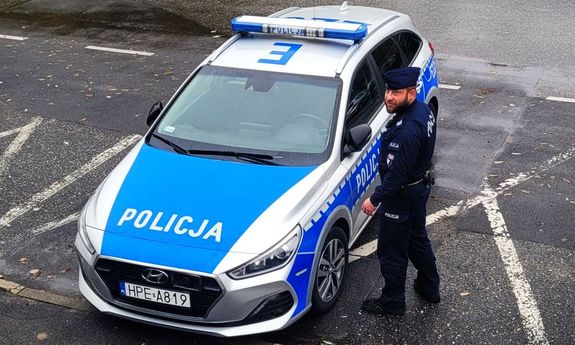 Umundurowany policjant stoi obok oznakowanego radiowozu