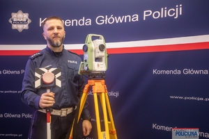 policjant stoi na tle rollupu z napisem Komenda Główna Policji obok niego stoi urządzenie na stojaku