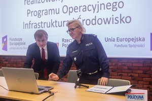 policjantka i mężczyzna w garniturze stoją przy stole patrząc w ekran laptopa