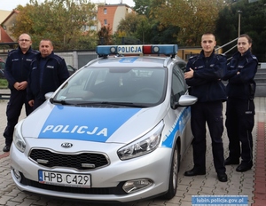 trzej policjanci i policjantka stoją przy radiowozie