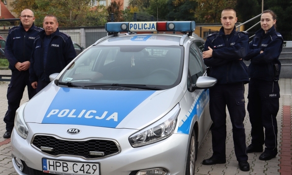 trzej policjanci i policjantka stoją przy radiowozie