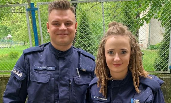 Policjant i policjantka stoją na tle zielonych roślin