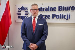 Na tle napisu Centralne Biuro Śledcze Policji stoi mężczyzna ubrany w granatowy garnitur