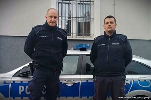 dwóch umundurowanych policjantów stoi przy radiowozie