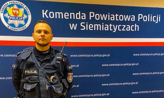 Policjant stoi na tle napisu komenda powiatowa policji w Siemiatyczach