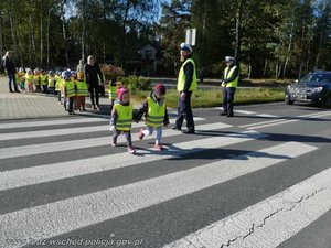 Policjanci przeprowadzają przez pasy dzieci ubrane w odblaskowe elementy