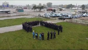 Policjanci na torze Słomczyn przechodzą szkolenie. Grupa policjantów stoi na trawie, w tle na parkingu radiowozy