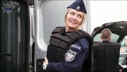 Policjantka ubiera kamizelkę na mundur i uśmiecha się za kamerę