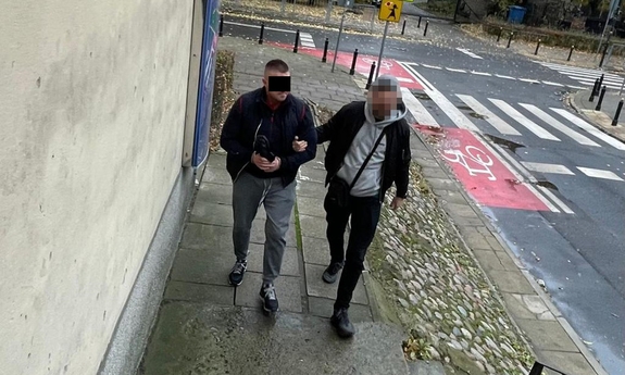 Nieumundurowany policjant prowadzi zatrzymanego mężczyznę.